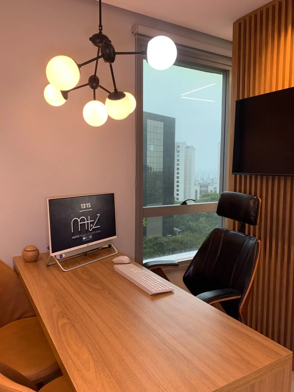 Sala de reunião da clínica, com mesa, monitor e vista para a avenida
